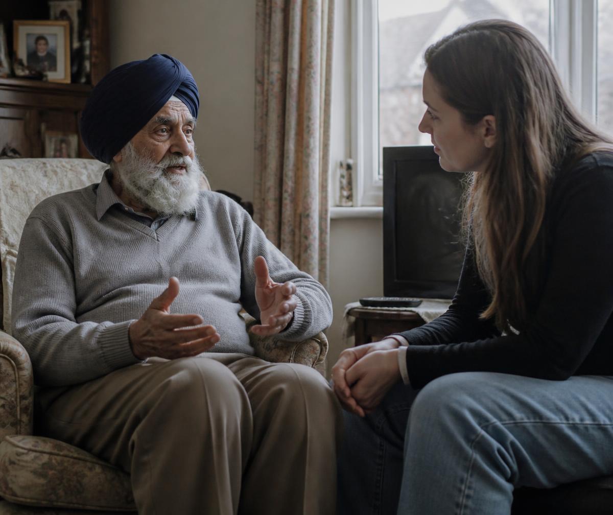 A companion listening attentively to an older Sikh gentleman in his living room