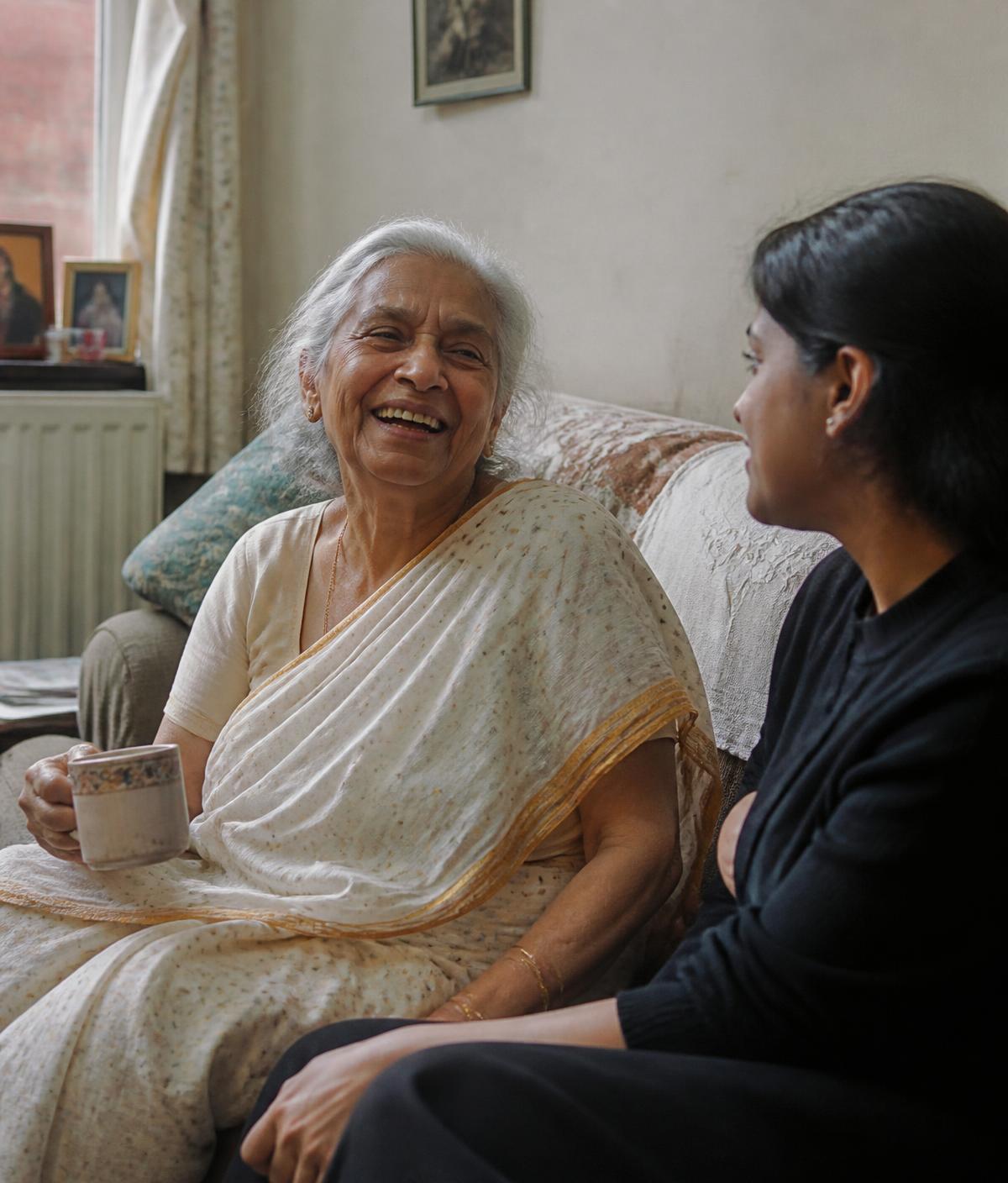 An older South Asian woman laughing with her SAATH companion over a cup of tea at home
